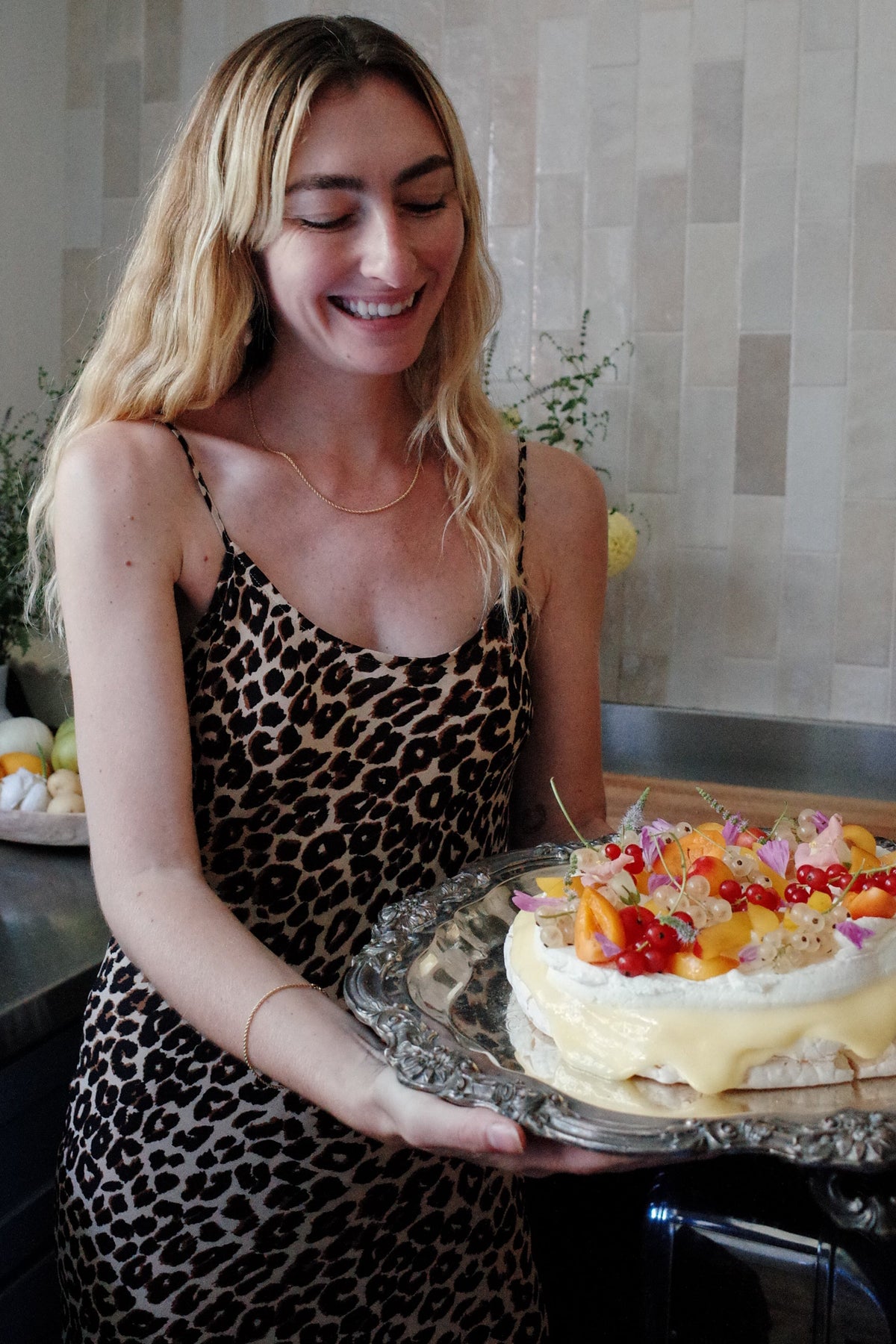 A woman wearing an Odissea 14k gold rope chain necklace and matching bracelet while holding a fruit pavlova cake.