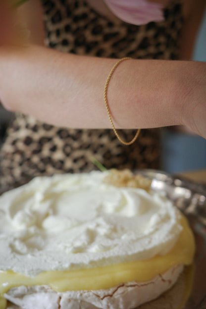 Odissea 14k gold rope chain bracelet worn on a wrist above a cream-topped dessert