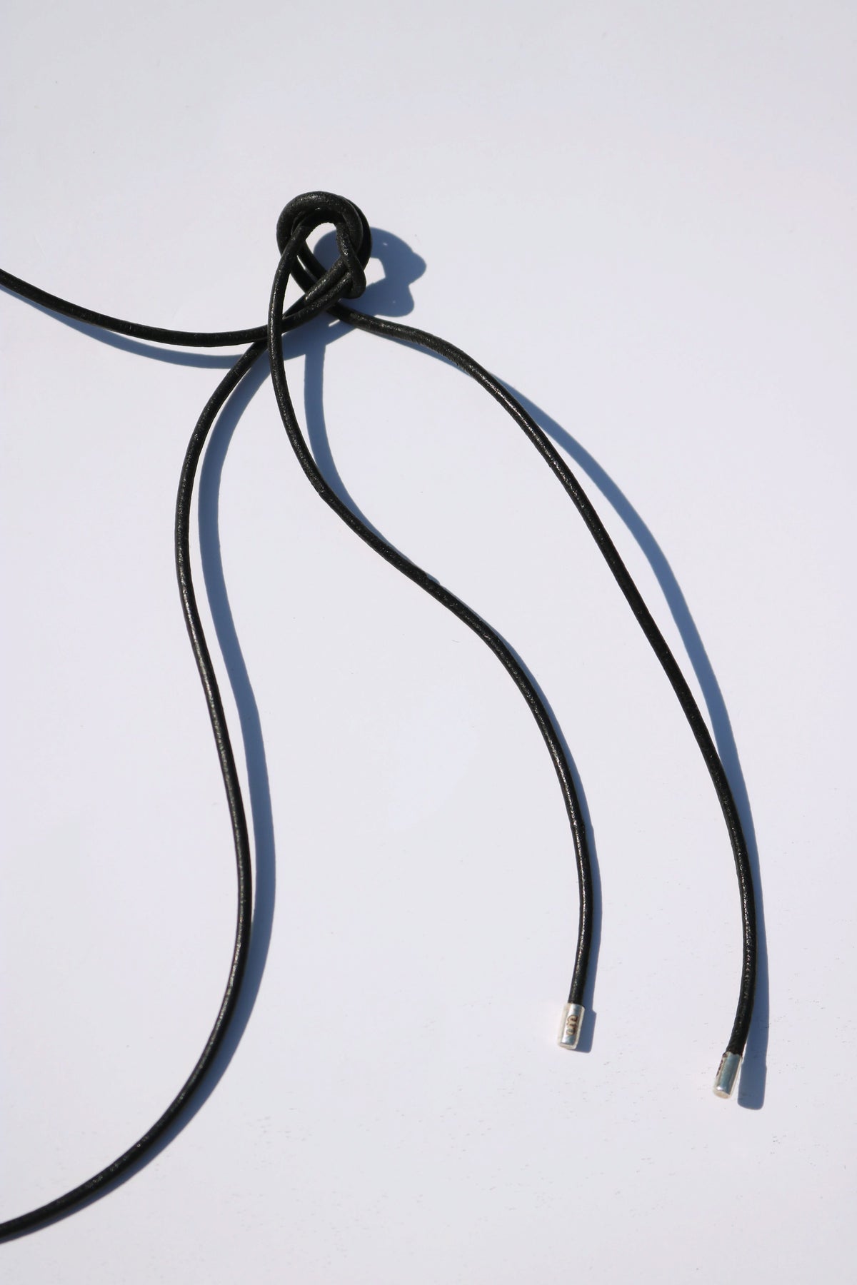 Odissea black leather barrel necklace cord with silver tips and a decorative knot detail on a white background