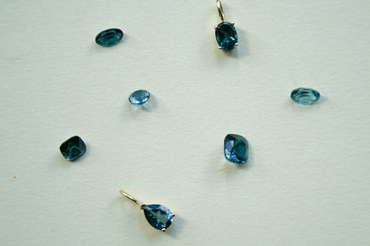 Odissea blue topaz pendants in 14k yellow gold with various stone cuts on a textured white background