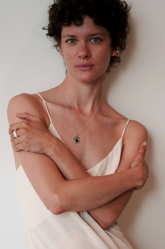Odissea Helios pendant in 14k white gold with blue tourmaline on a 17-inch chain worn by a woman in a cream dress